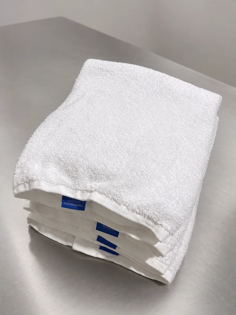 A stack of folded white bath towels with blue eWASH labels